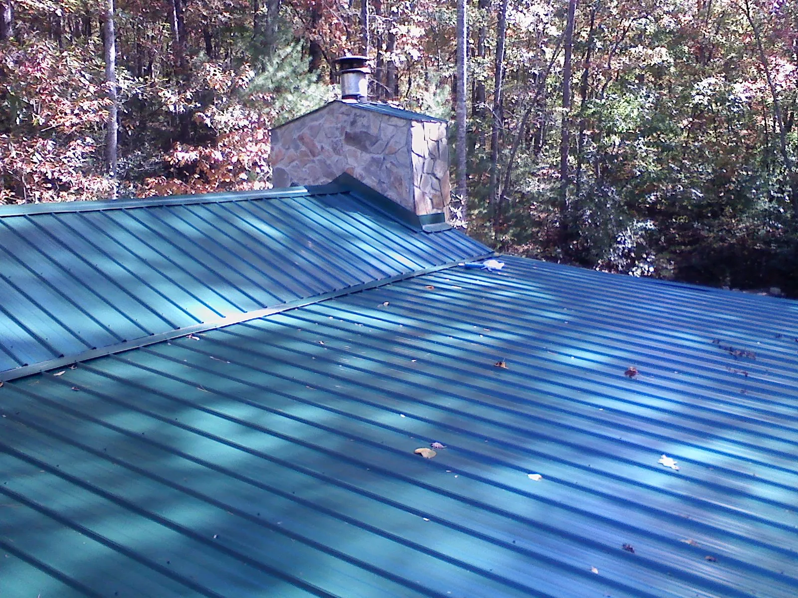 New green metal roof and stone chimney surrounded by autumn woods in Danville